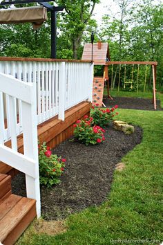 a wooden swing set and flower bed in the yard next to a white picket fence