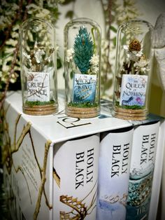 three bottles with plants in them sitting on top of a book shelf next to each other