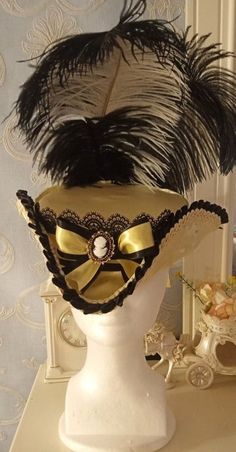 Marie Antoinette/ Rococo (or Late Baroque) Style Ladies Tricorn Hat in Buttercream Yellow Satin with Black Lace Accents & Ostrich Plumes.  This piece is 12.5 inches from front to back with a generous 6.85 inch crown diameter. In the front, sits a  Classical Style Silhouette Cameo Brooch (the height of fashion in the mid-late 18th Century) on top of a satin bow against black lace. The back of this elegant, ultra-feminine piece is adorned with matching grograin & satin ribbons topped with luxurious black & white Ostrich plumes. The outer side of this hat is edged in high profile (thick), scalloped edge braided gimp trim in pale yellow and is paired with a pale yellow scroll braided gimp trim on the inside. Usually, I sew both an elastic band and/or matching side ribbons into the lining of th Rococo Hat, Rococo Fashion Modern, Tricorn Hat, Rococo Dress, Rococo Fashion, Yellow Satin, Satin Ribbons, Ultra Feminine, Classical Style