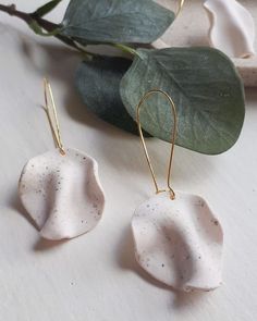 two white ceramic earrings with gold ear wires on top of a table next to a plant