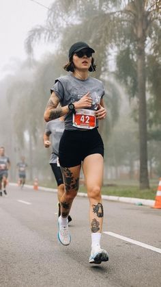 a woman running down the road with tattoos on her arm and leg, while wearing a hat