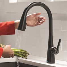 a person is washing asparagus in a kitchen sink with the faucet running