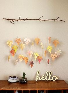 an arrangement of autumn leaves arranged on a wall with a branch in the middle and another leaf hanging above it