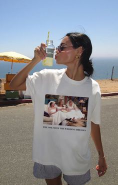 a woman drinking from a water bottle while standing on the side of the road