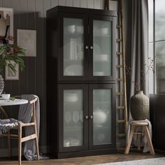 a tall black cabinet with glass doors in a living room next to a table and chair