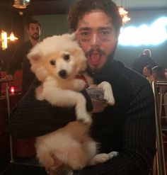 a man holding a small white dog in his arms while standing next to another person