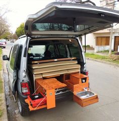 the back end of a van with an open hatchback and wooden furniture in it