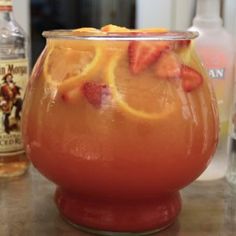 a drink in a glass with orange slices and strawberries on the rim next to bottles