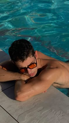 a man in sunglasses laying on the edge of a swimming pool