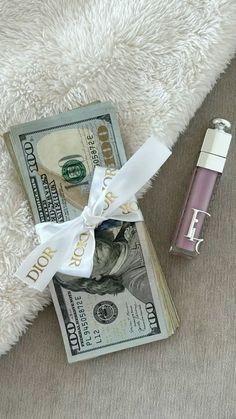 a roll of money sitting on top of a white blanket next to a tube of lipstick