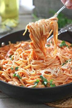 someone is holding a fork full of spaghetti in a skillet with parsley on top