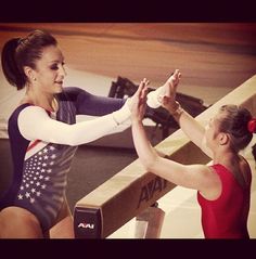 two women high fiving each other in an indoor gymnastics ring with one holding the other's hand