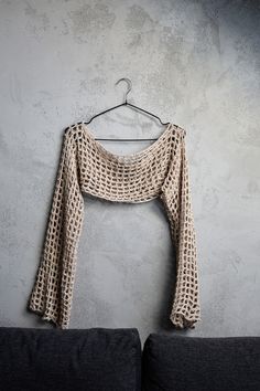 a crocheted sweater hangs on a hanger in front of a gray wall