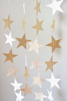 paper stars are hanging from the ceiling in front of a white wall with gold foil on it