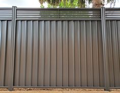 a large metal fence is shown in front of a tree and some dirt on the ground