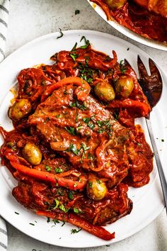 a white plate topped with meat and veggies covered in sauce next to a fork