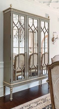 a dining room table and chairs in front of a mirrored cabinet with ornate carvings on the doors