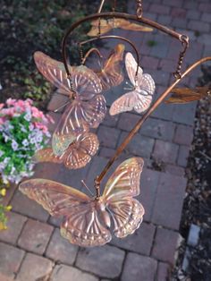 three butterfly wind chime hanging from a metal rod with flowers in the back ground