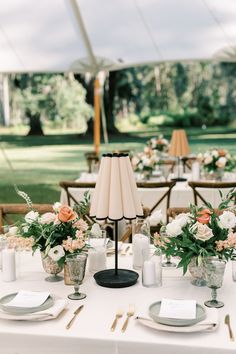 the table is set with flowers and candles for an outdoor wedding reception in a tent