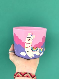 a hand holding a pink and purple cup with an image of a llama on it