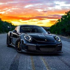 a black sports car driving down the road at sunset