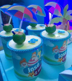 three ice cream cups with apples and umbrellas in them sitting on a blue table