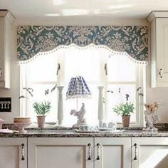 a kitchen with white cabinets and an ornate window valance over the sink, along with potted plants