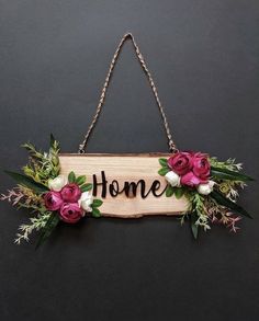 a sign that says home with flowers hanging from it's side on a chain