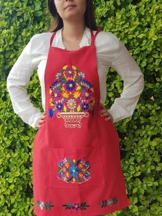 a woman standing in front of a bush wearing an apron with colorful flowers on it