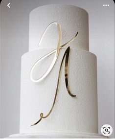 a three tiered white wedding cake with gold monogramming