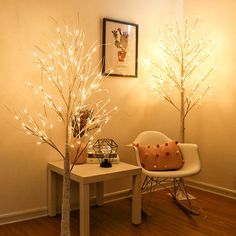 two small trees with white lights are in the corner of a room next to a chair