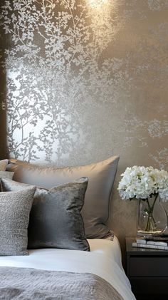 Elegant metallic wallpaper accent wall in silver and gold, with neatly made bed, soft grey pillows, white flowers, glass Luxurious Bedroom Wallpaper, Gray Wallpaper For Bedroom, Silver And Cream Bedroom, Metallic Wallpaper Accent Wall, Wall Ideas For Bedroom, Grey And Silver Bedroom Ideas, Wallpaper Ideas For Bedroom, Sleek Nightstand, Wallpaper Accent Wall Ideas