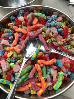 a bowl filled with lots of different colored candies on top of a table next to two spoons