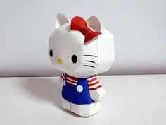 a white hello kitty figurine with a red bow on its head and blue dress