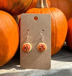 a pair of orange pumpkin earrings sitting on top of a wooden table next to some pumpkins