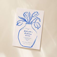 a blue vase filled with flowers on top of a white sheet covered tablecloth next to a card