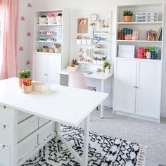 a white desk sitting in the middle of a living room next to a pink curtain