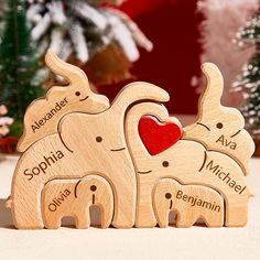 three wooden elephants with names on them and a red heart in the middle, surrounded by christmas trees