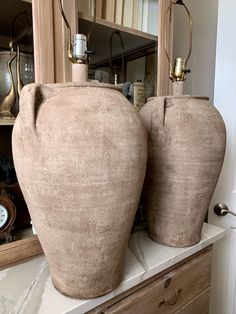 two large vases sitting on top of a counter next to a clock and mirror