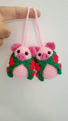 two small crocheted pink pigs hanging from a string on a white wall next to a persons hand