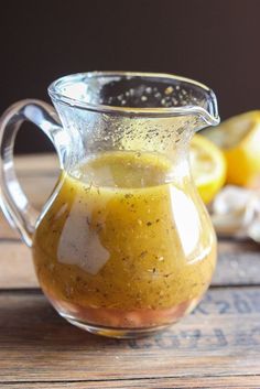 a glass pitcher filled with liquid sitting on top of a wooden table next to sliced lemons