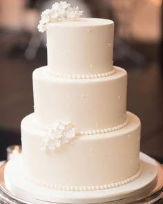 a three tiered white wedding cake with pearls and flowers on the top, sitting on a silver platter