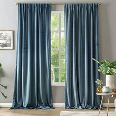 a living room with blue curtains and a white couch in front of a window that has a potted plant next to it