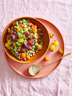 a pink plate topped with a salad next to two spoons on top of a table