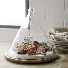 a platter with meats and vegetables under a glass dome on a counter top