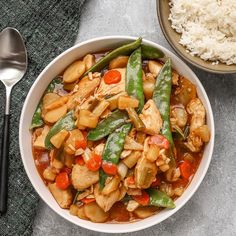 a white bowl filled with chicken and veggies next to rice on a table