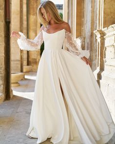 a woman in a white wedding dress standing on a stone floor with her arms outstretched