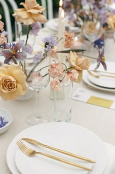 the table is set with white plates and silverware, flowers in vases, and candles