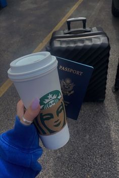 a person holding up a starbucks cup next to a suitcase on the street with their passport