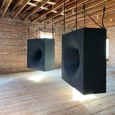 two large speakers are suspended from the ceiling in an empty room with exposed wood flooring